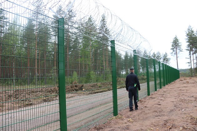 Vihreä esteaita jonka vieressä kävelee rajavartija.