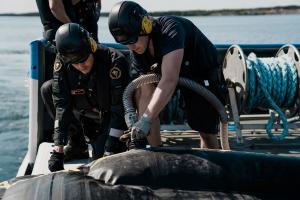 Två personer installerar en slang på fartygets däck för oljebekämpning.